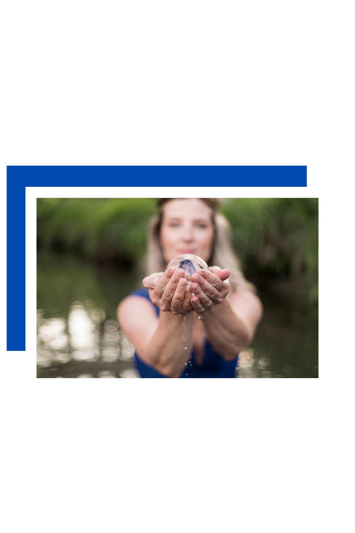 Woman holding a water globe, standing outdoors near water with lush greenery in the background.
