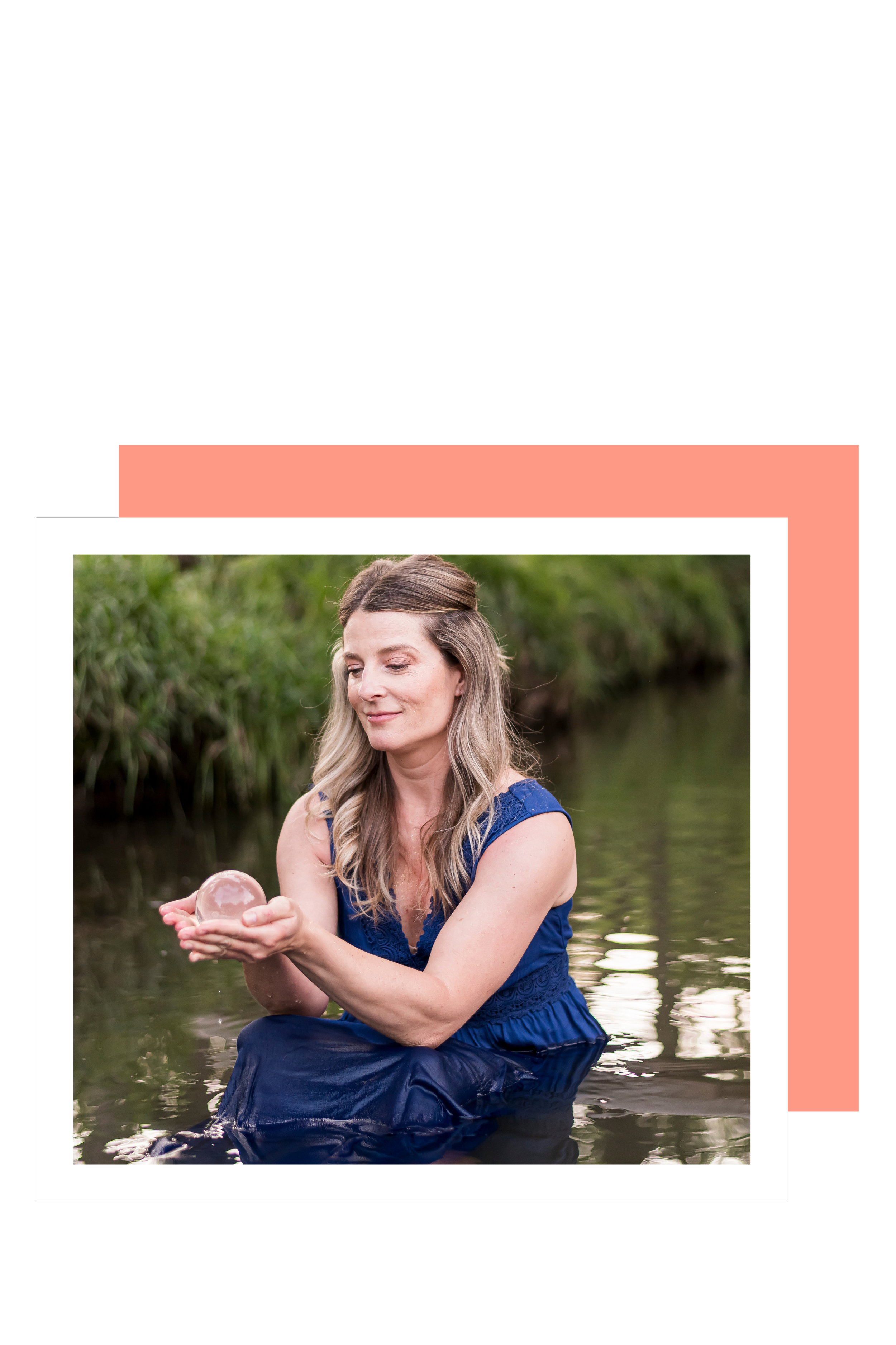 A woman in a blue dress sitting in shallow water, holding a clear glass sphere, with green foliage in the background.