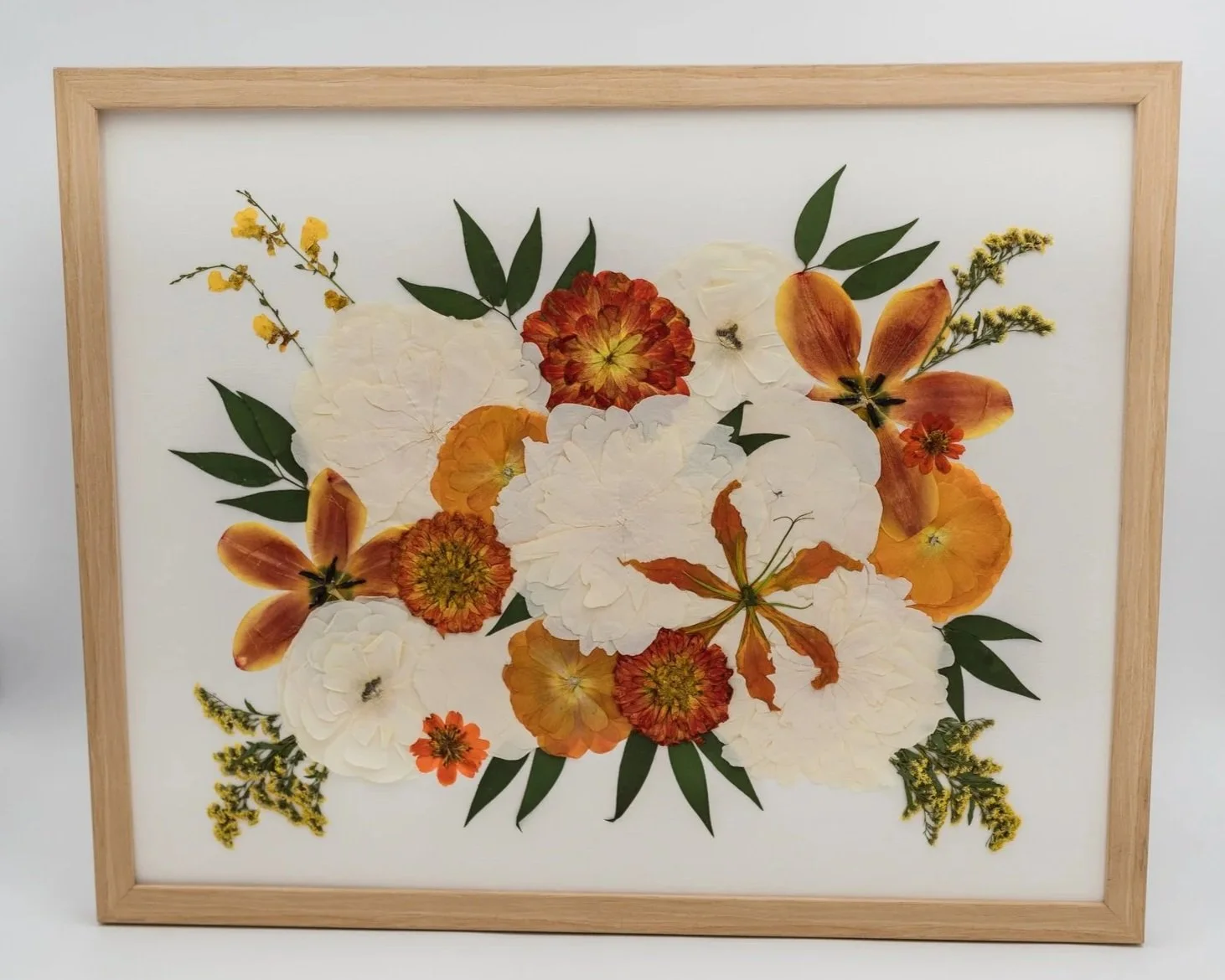 Pressed flower arrangement with white, orange, yellow, and red flowers in a wooden frame.
