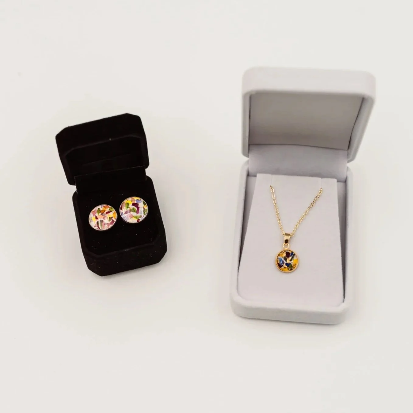 A pair of colorful circular earrings in a black jewelry box, and a matching necklace with a circular pendant in a white jewelry box.
