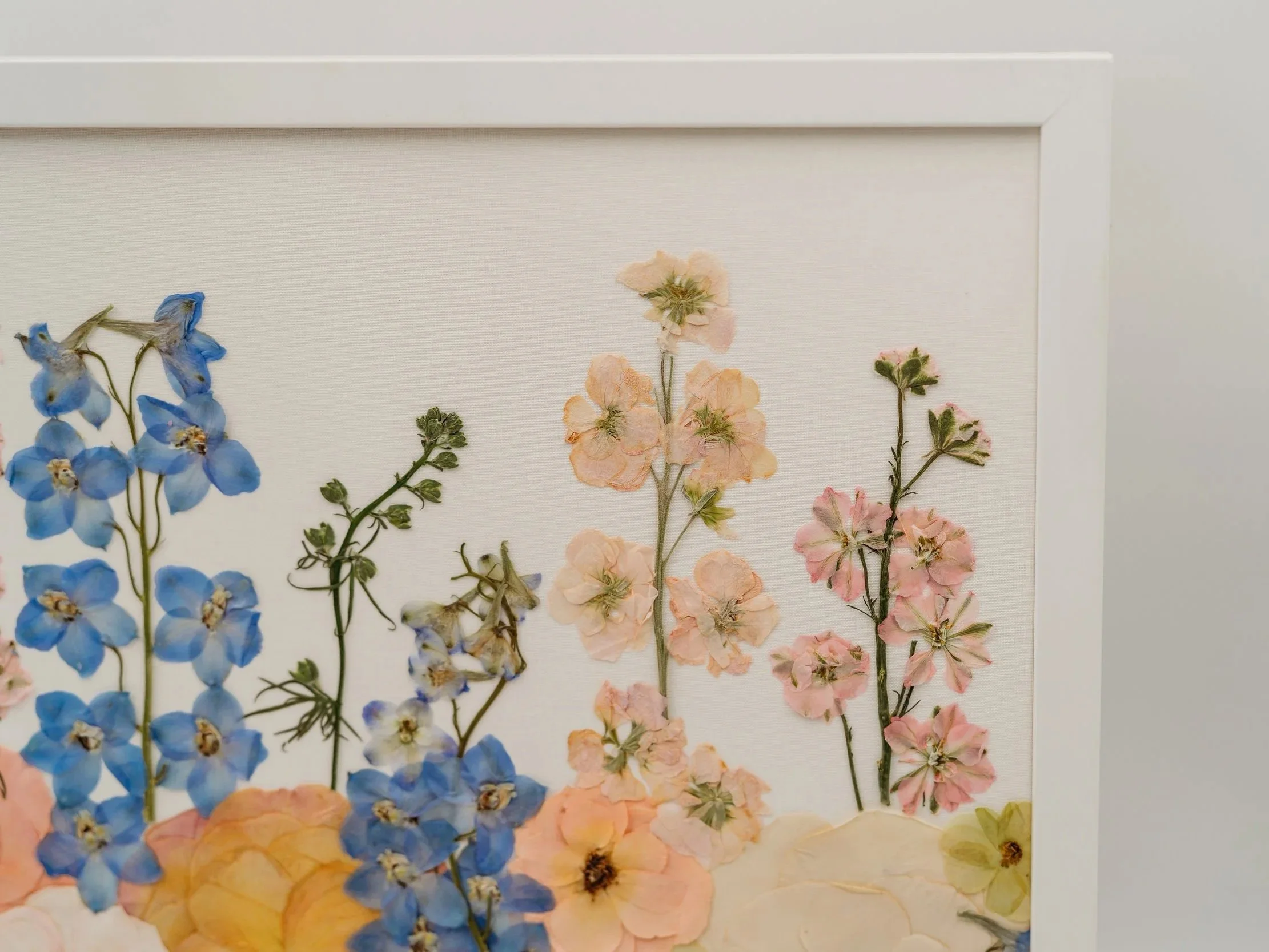 Pressed flower art featuring blue, pink, and peach flowers arranged vertically on a white background.