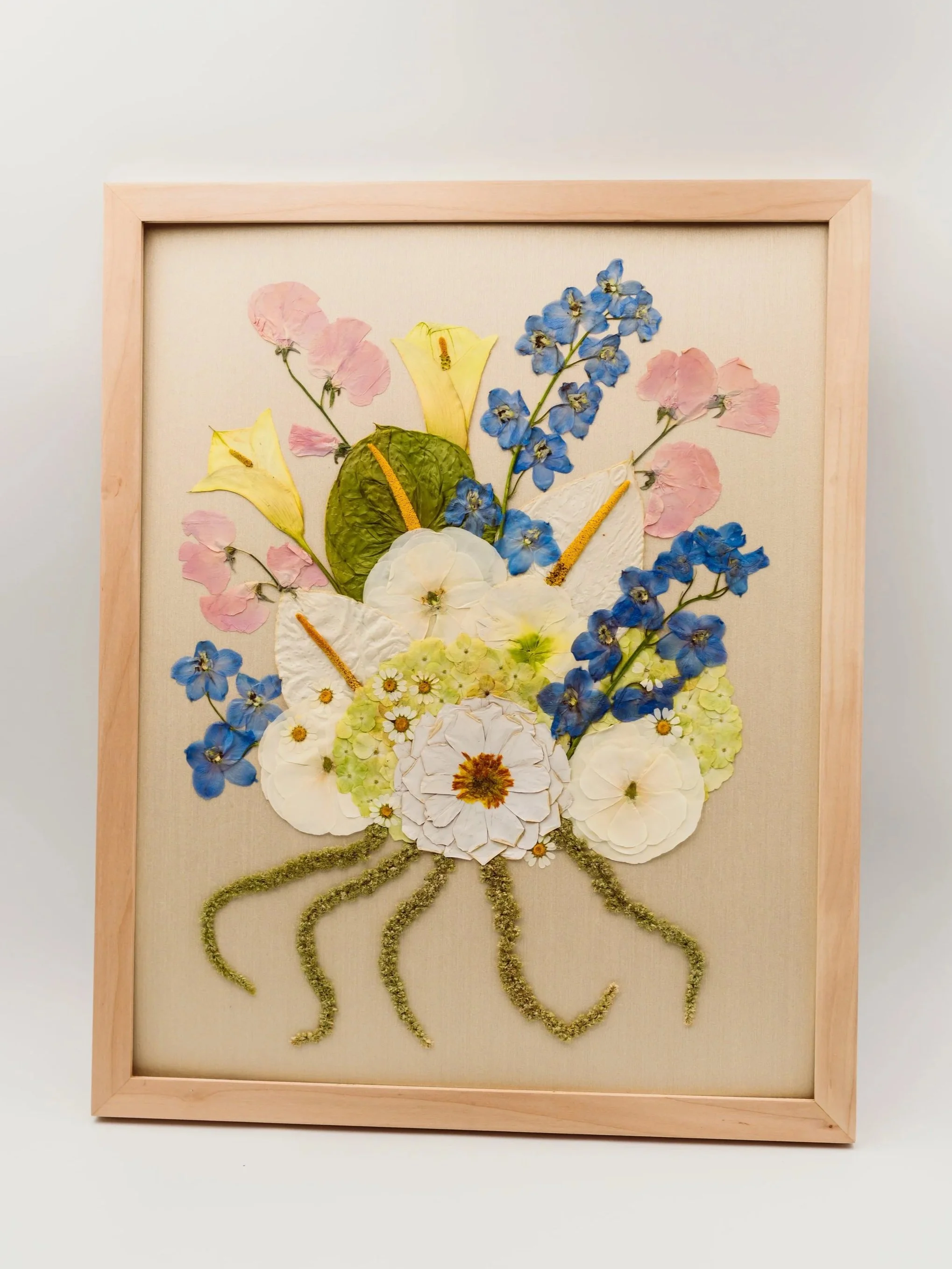 A framed artwork of a butterfly made from pressed and dried flowers with a beige background.
