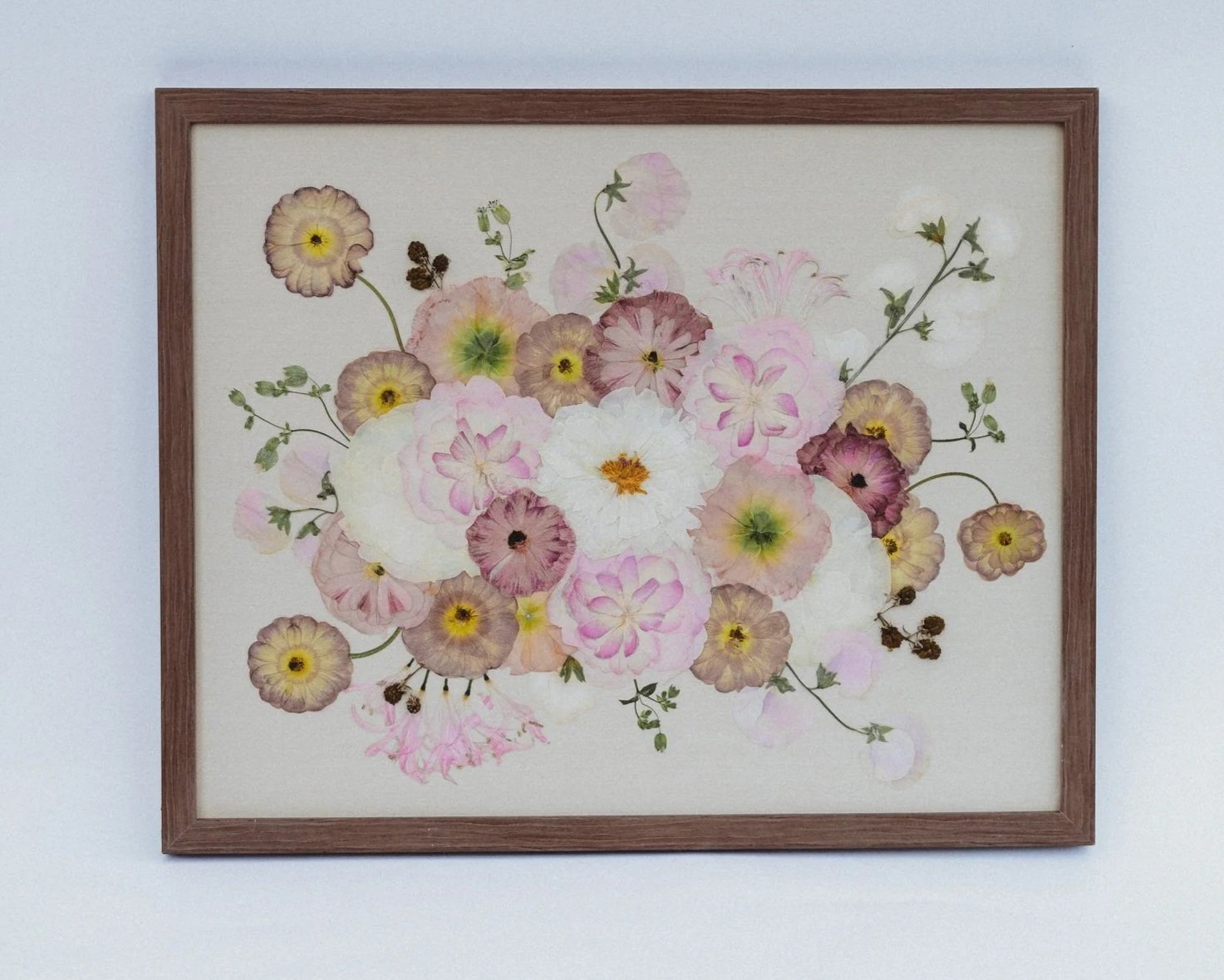 A framed watercolor painting of a bouquet of various pink, white, and purple flowers with green leaves and stems on a neutral background.