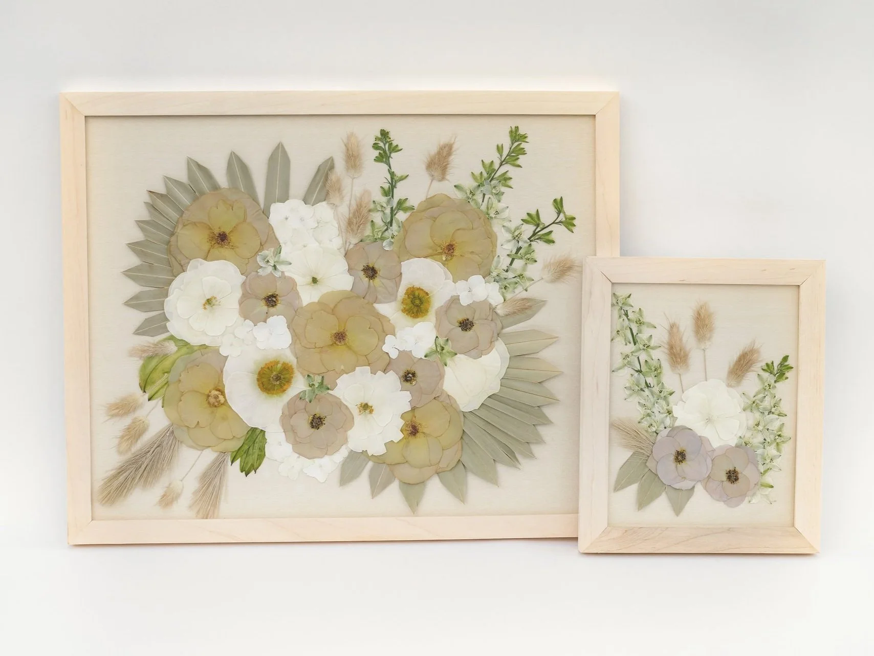 Two framed botanical art pieces with dried flowers and leaves arranged in flower shapes, against a white background.