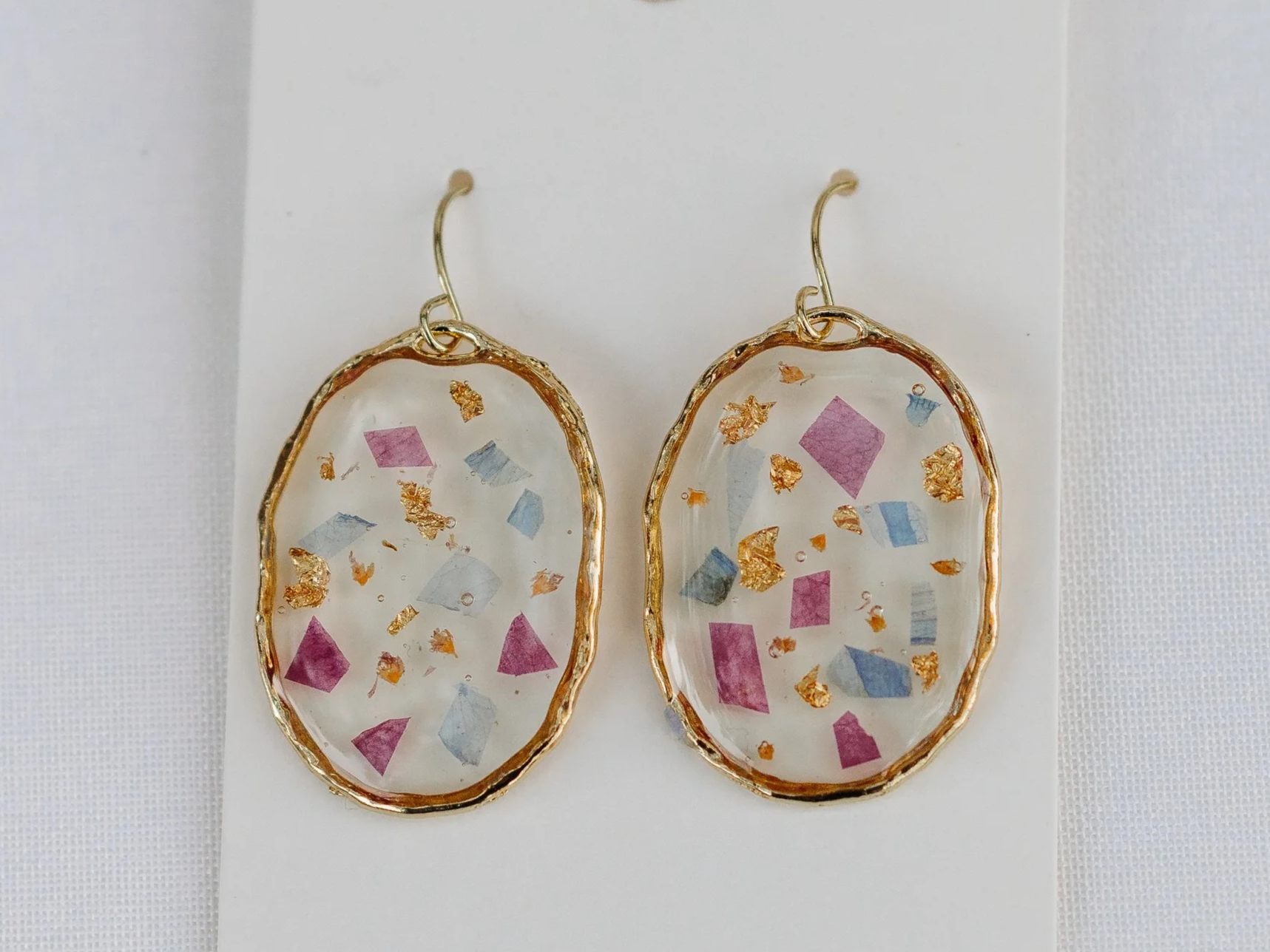 Display of earrings with pressed flowers on brown paper backing, arranged on a wooden surface.