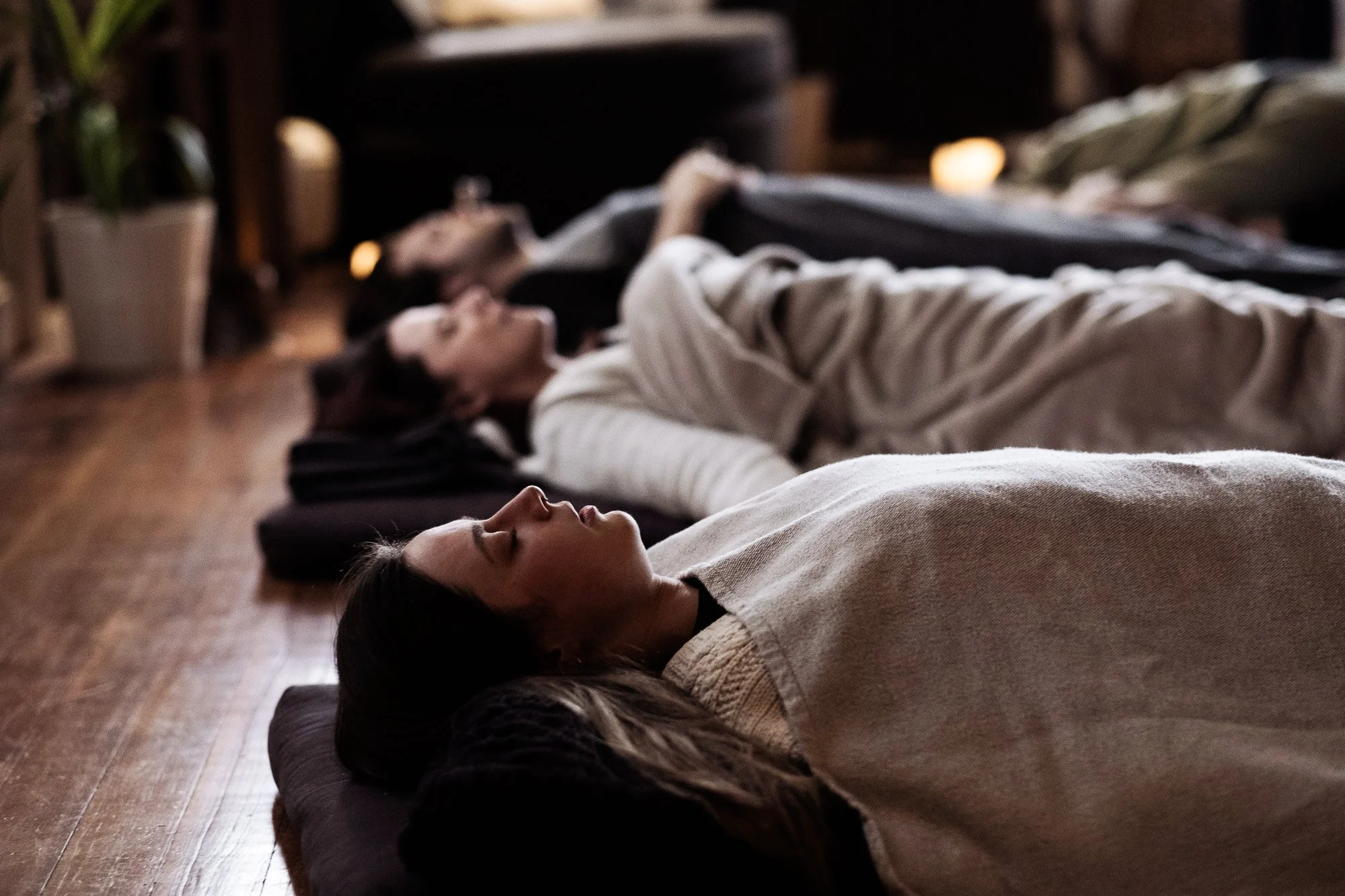 Group of people lying on cushions on the floor in a dimly lit room, appearing to be relaxing or meditating.