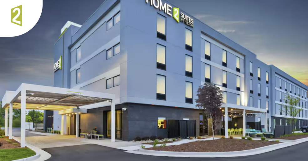 Modern house on a grassy hillside with snow-capped mountains and cloudy sky in the background.