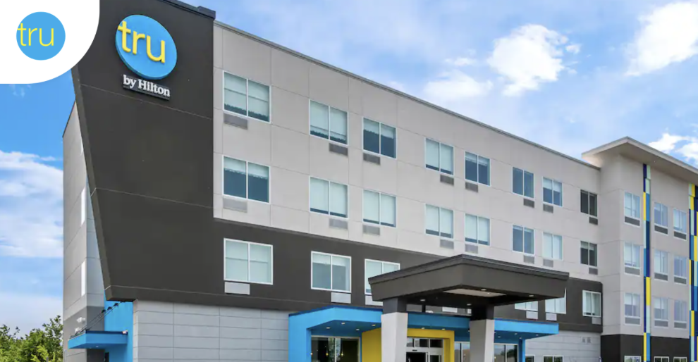 A scenic landscape with a lake, rolling hills, and mountains under a cloudy sky.