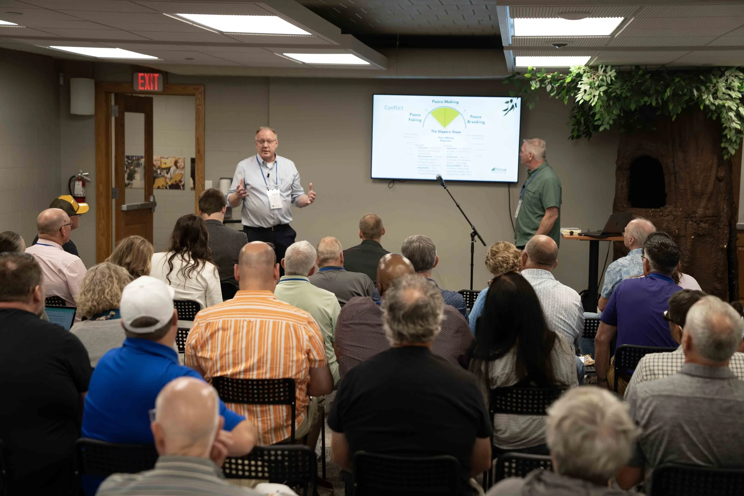 Group of people sitting in chairs in a conference room, some engaged in prayer or an emotional moment.