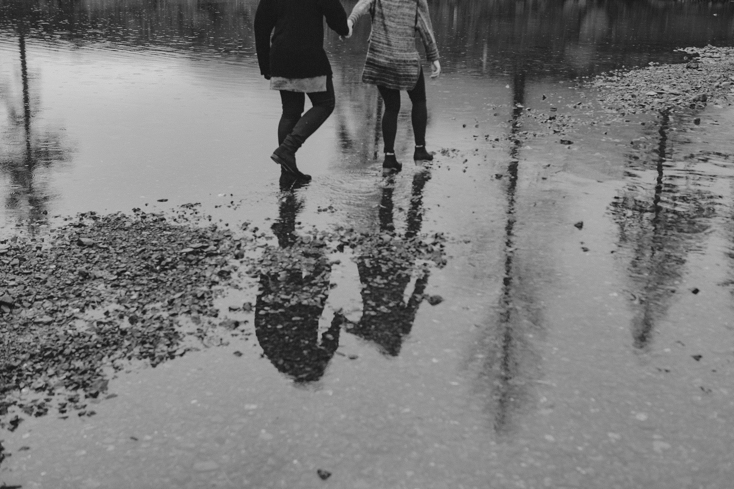 Two people walking on a wet surface with reflections visible.