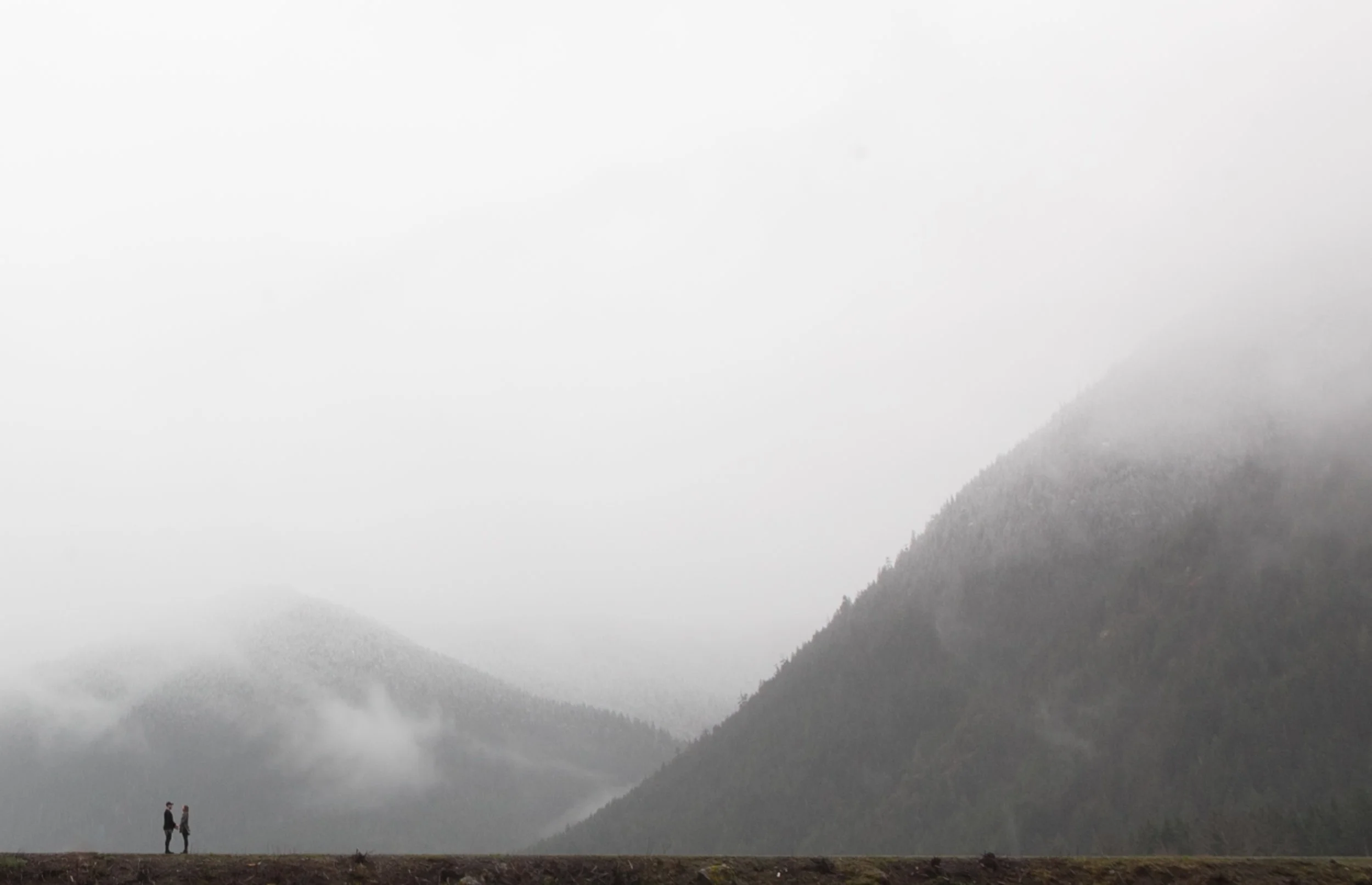 Two people standing on a hill with misty mountains in the background.