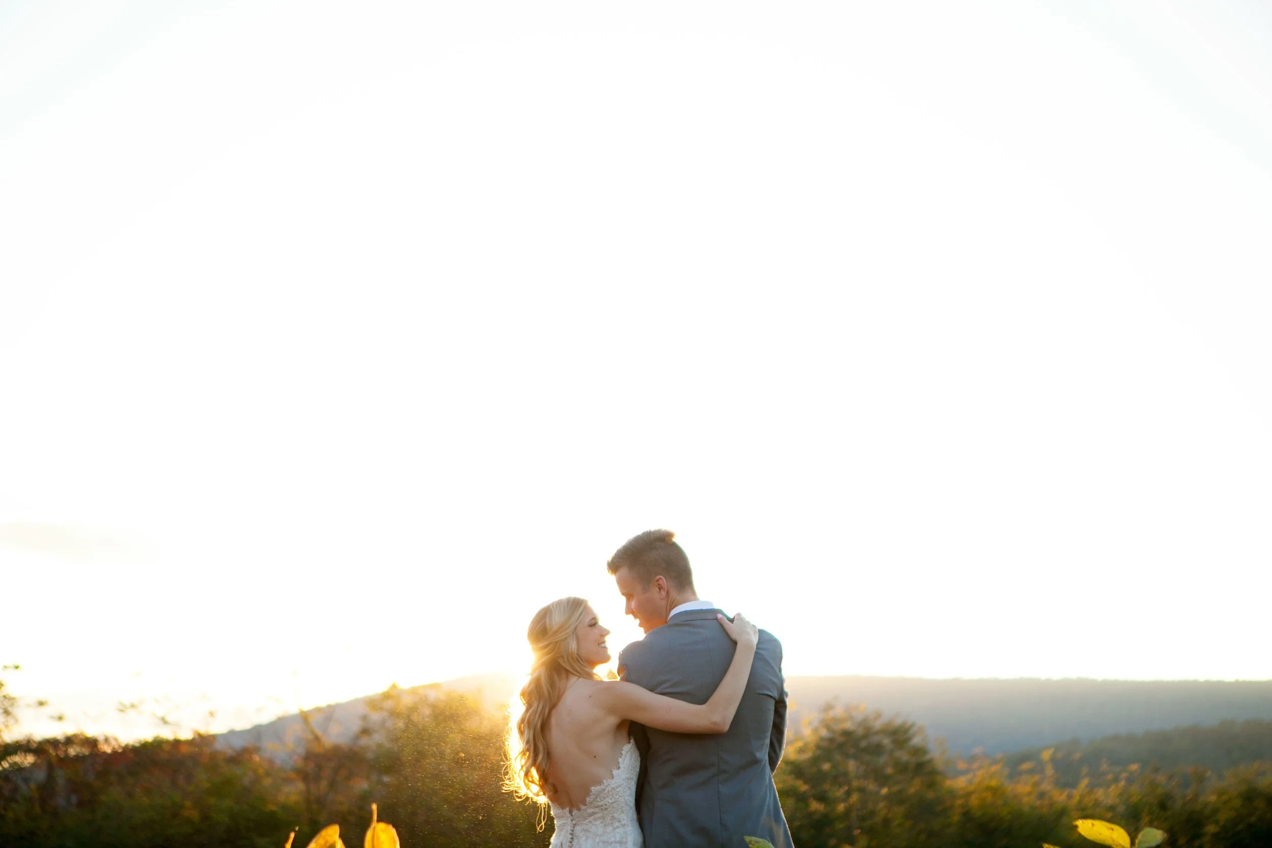 Couple embracing during sunset outdoors, woman in bridal gown and man in suit.