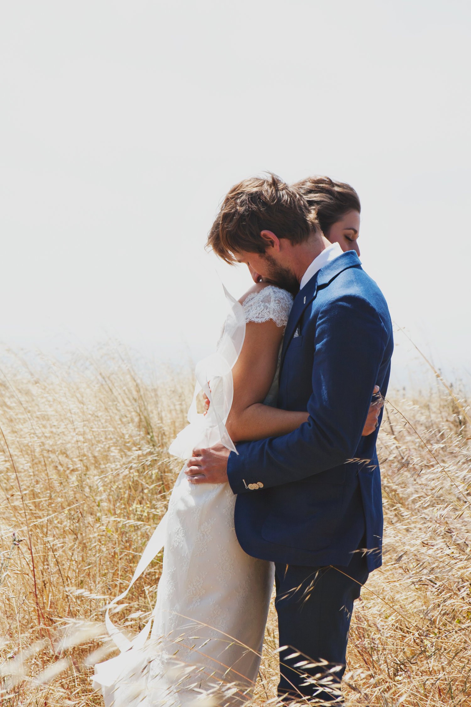 Bride and groom embracing in a field with tall grass