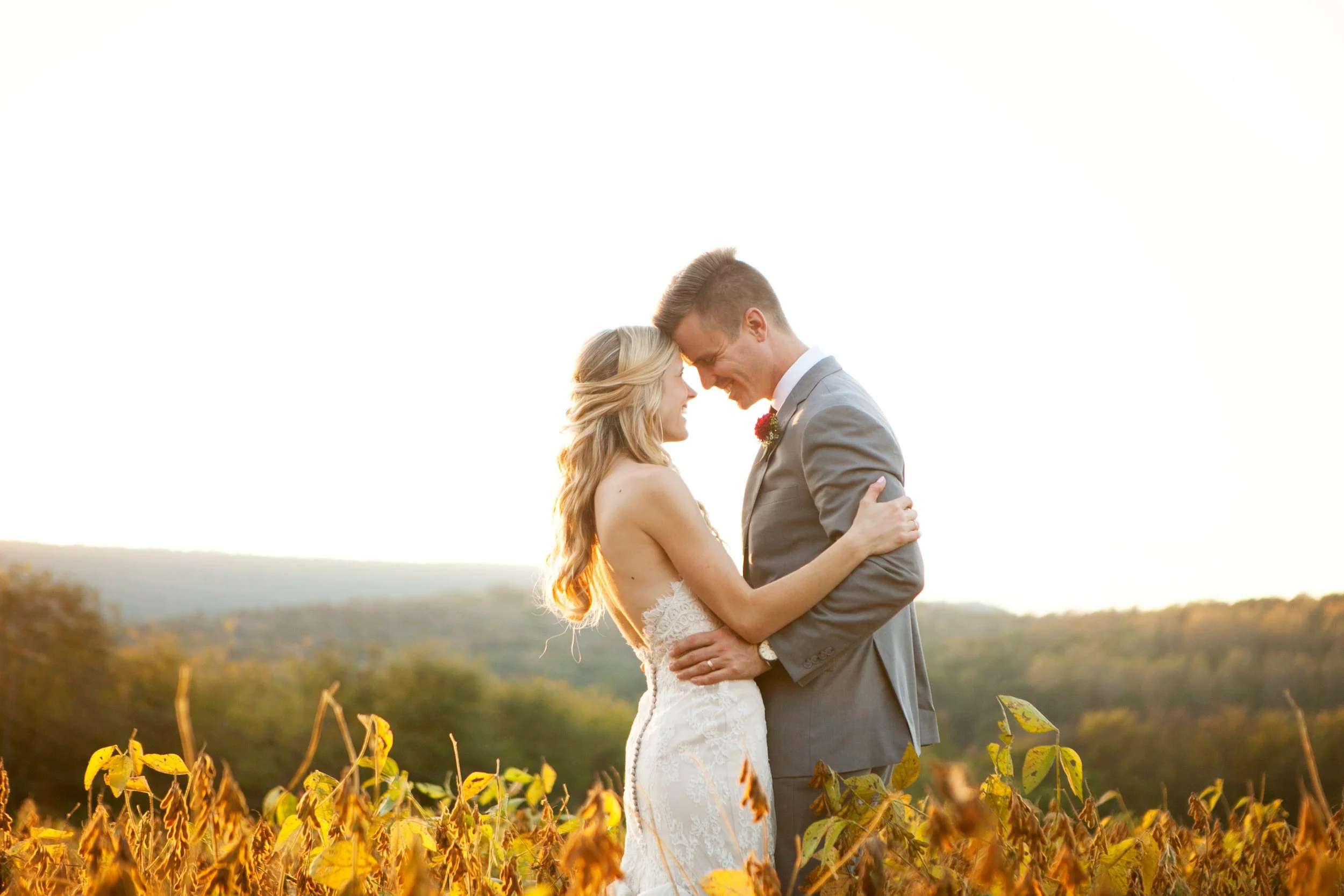 Bride and groom embracing in a field during sunset.