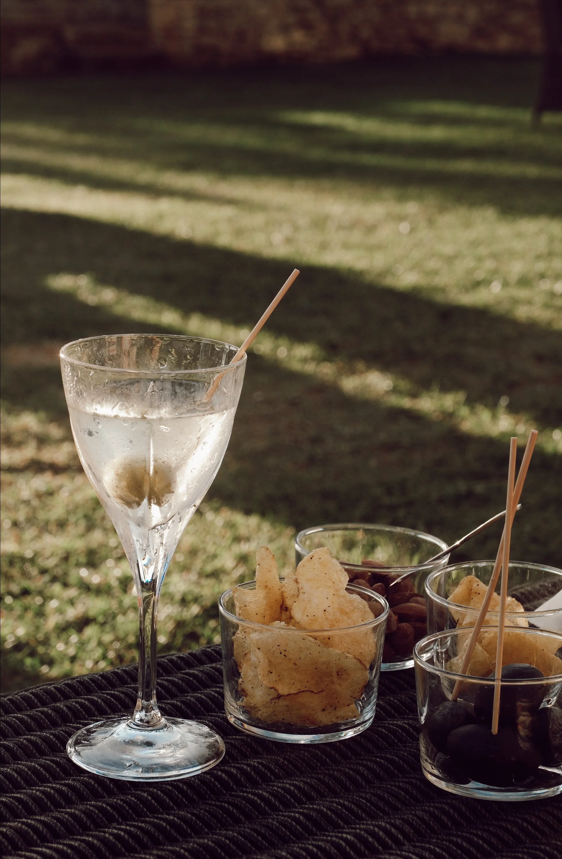 Martini glass with olive, snacks in bowls on outdoor table.