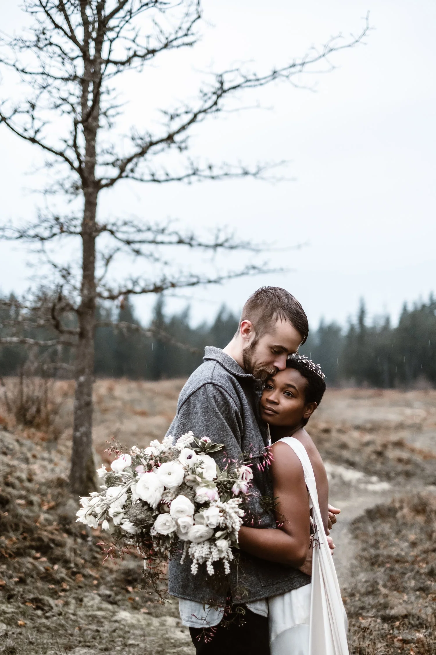 Couple embracing outdoors with bouquet, tree in background