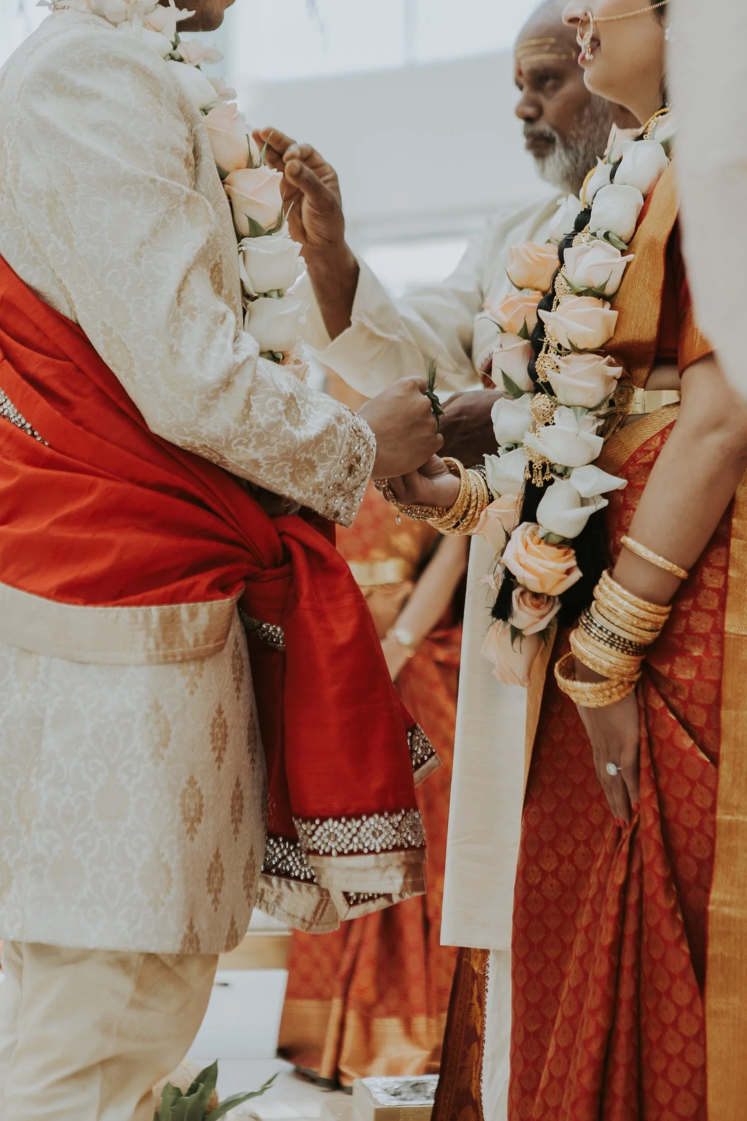 Traditional Indian wedding ceremony with bride and groom in ornate attire, exchanging flower garlands, surrounded by close-up details of their clothes and jewelry.