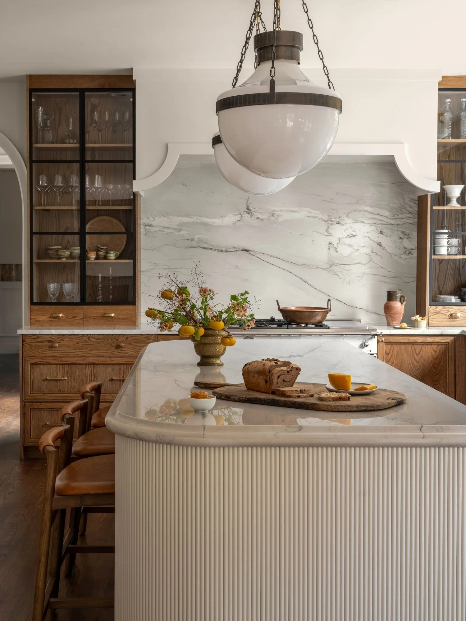 A modern farmhouse kitchen with a marble island, a bouquet of flowers, bread on a wooden board, and a hanging light fixture.