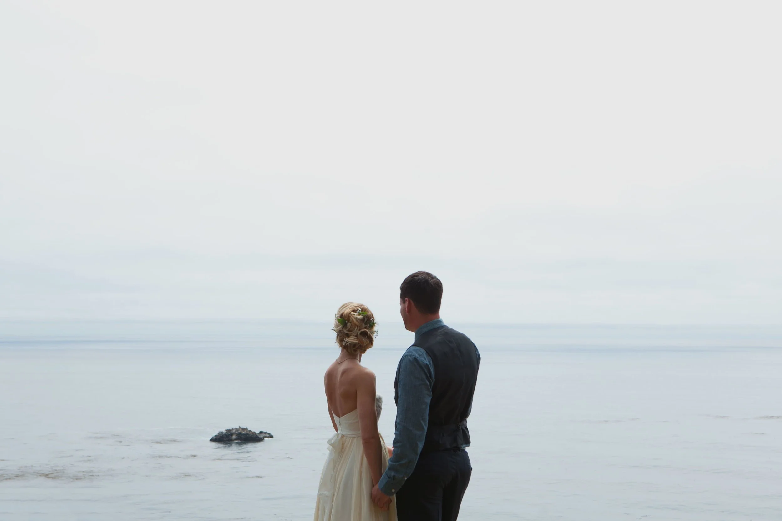 Couple in wedding attire holding hands by the ocean