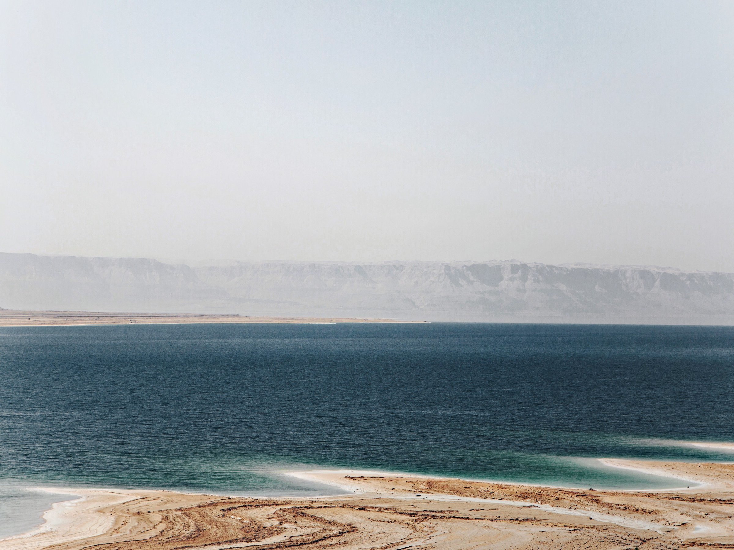 View of a vast, calm sea with distant hills on the horizon and sandy beaches in the foreground.