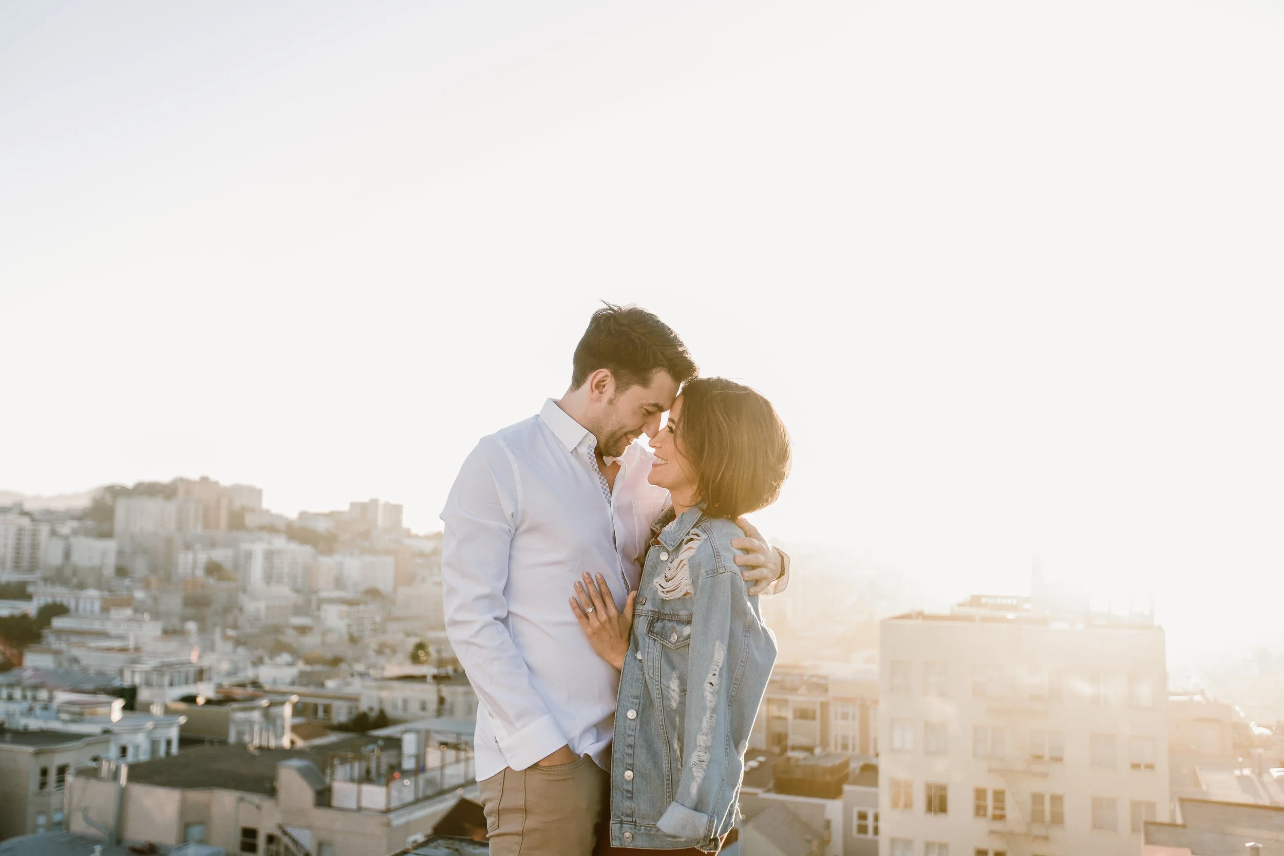 Couple embracing on a rooftop at sunset with city skyline in the background.