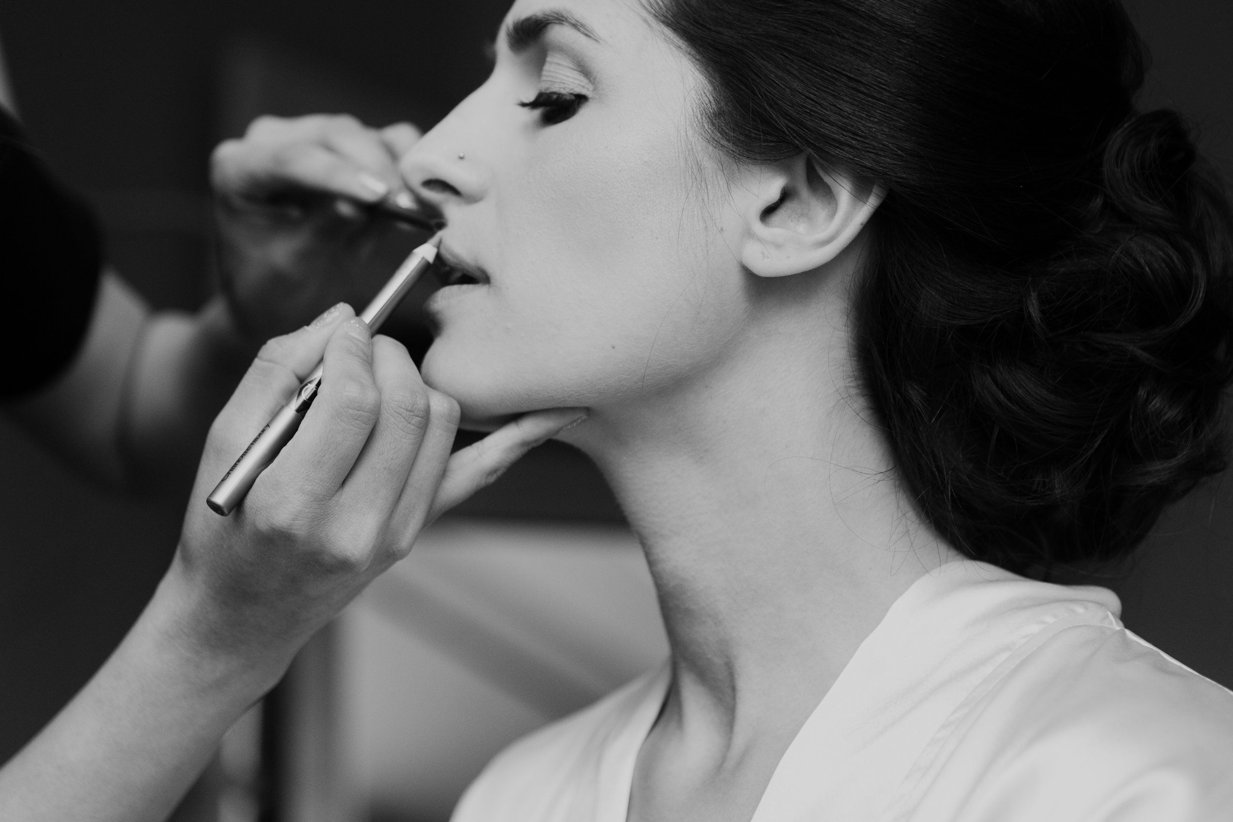 Makeup artist applying lipstick to a woman's lips in black and white.
