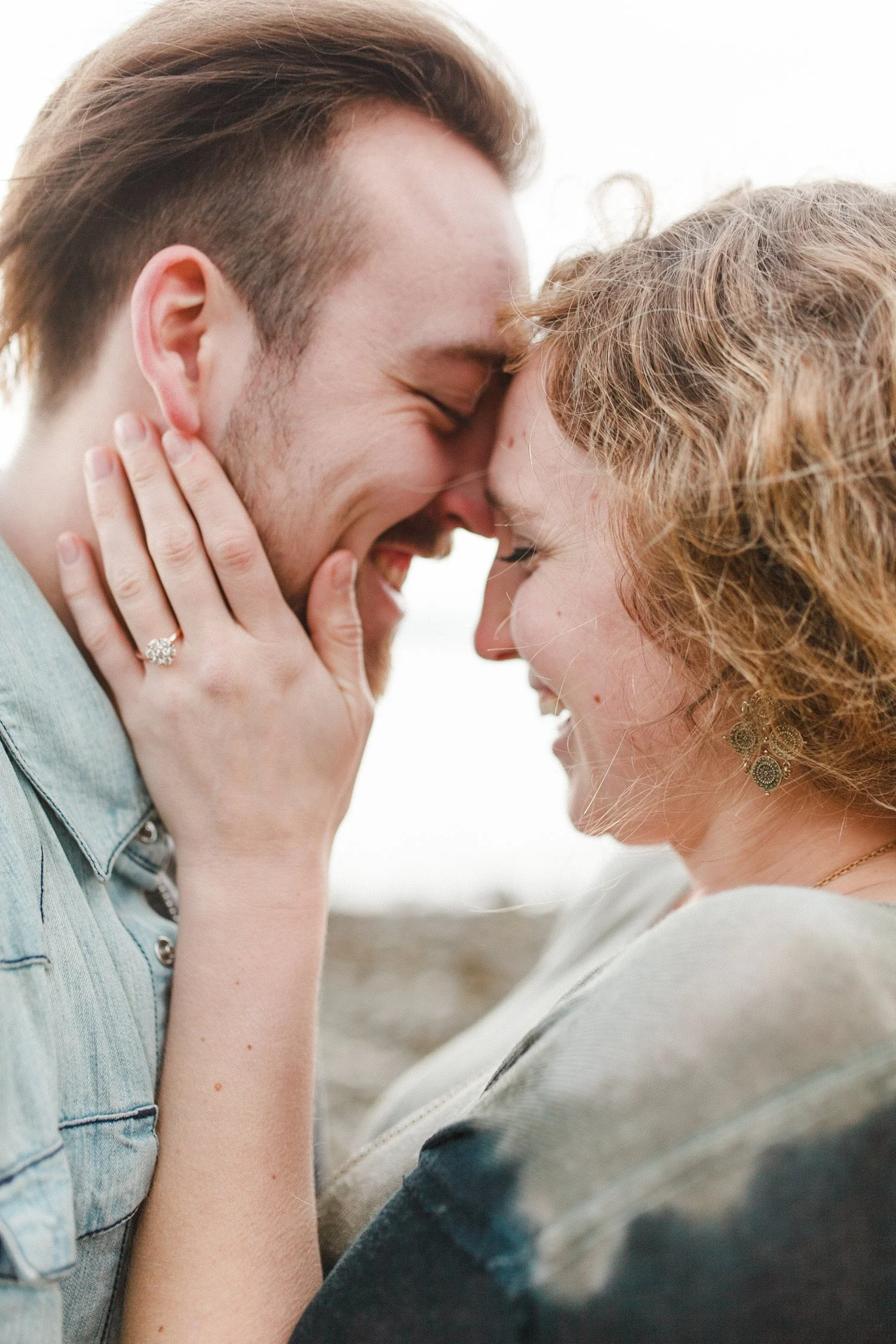 Close-up of a smiling couple touching foreheads, with the woman wearing a ring and earrings.