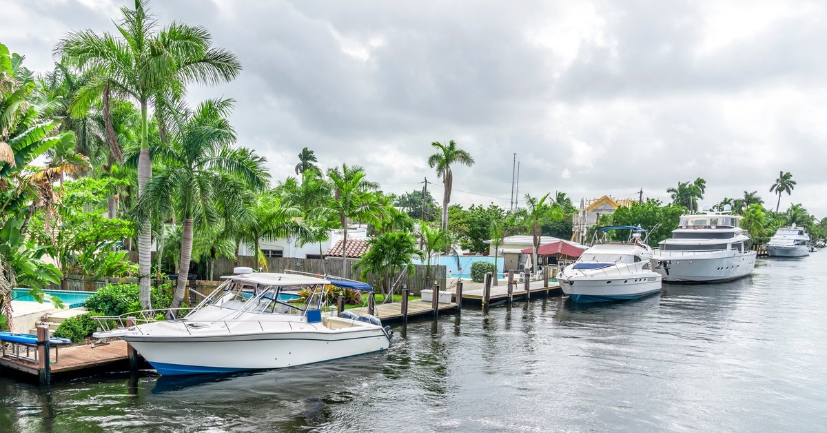 A neighborhood with palm trees featuring different houses with backyard boat docks. Multiple boats are docked on the water.