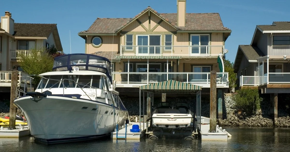 A home sits on the edge of the water with a small boat dock. There's a boat parked in the dock with a larger one beside it.
