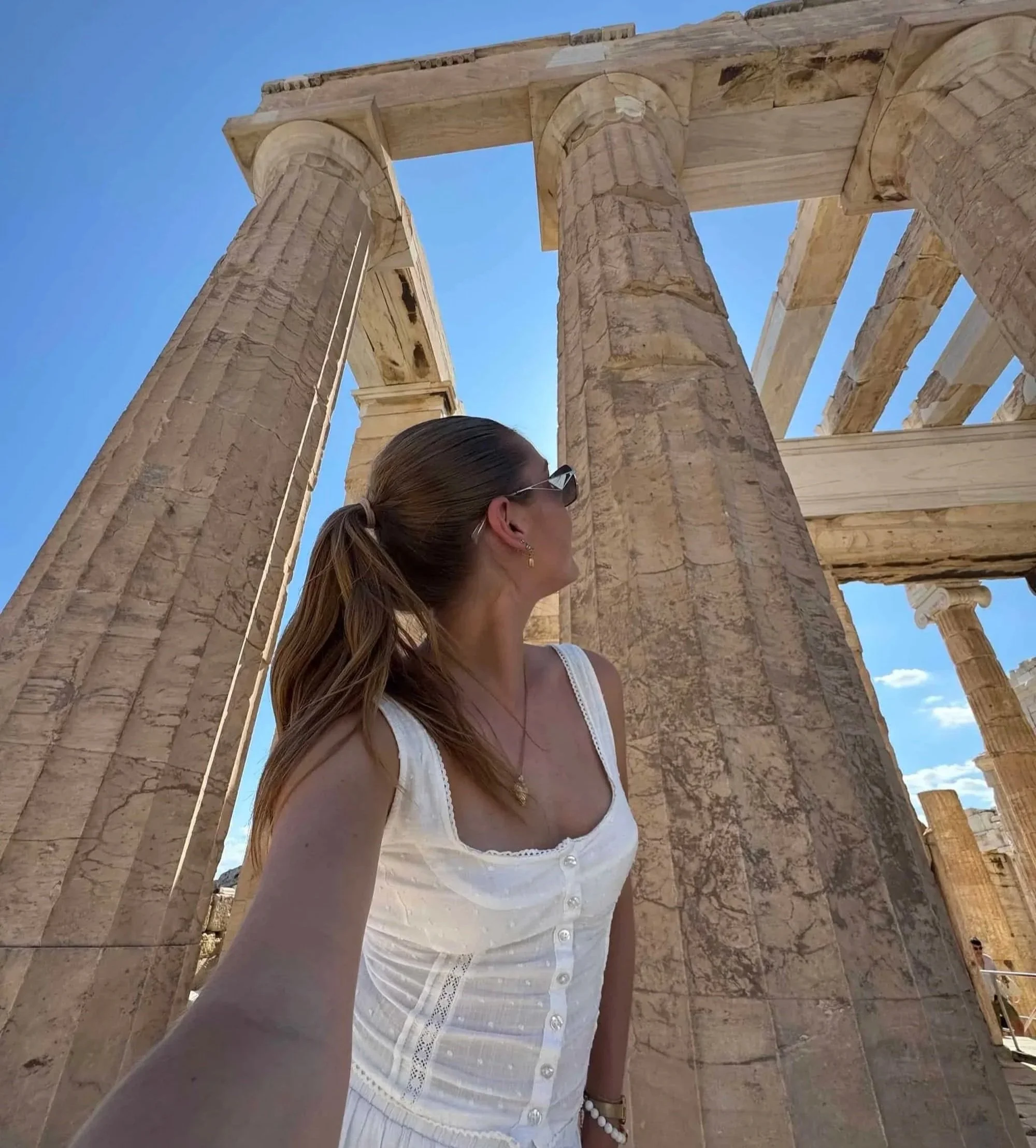 Woman in a white outfit admiring the ancient columns of the Acropolis—a must-see archaeological site for your Athens 2 day itinerary.