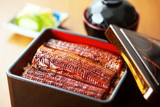 A lacquered box of glazed grilled eel (unagi) over rice, served with pickles and soup—a rich and savory Japanese food to try in Japan.