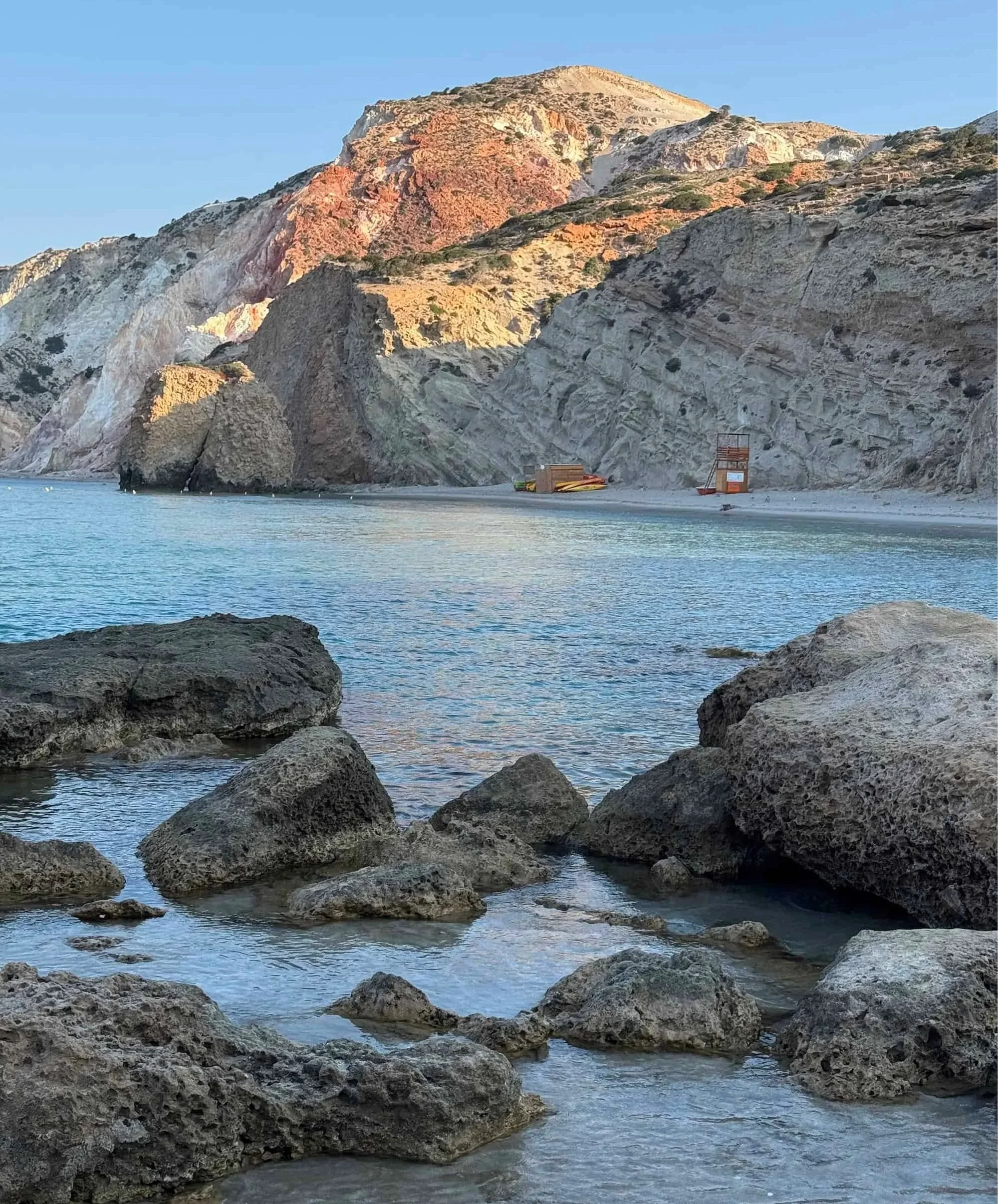 Waves lap against volcanic rocks beneath the dramatic red and white cliffs of Fyriplaka Beach—one of the most photogenic places to visit in Milos, Greece.