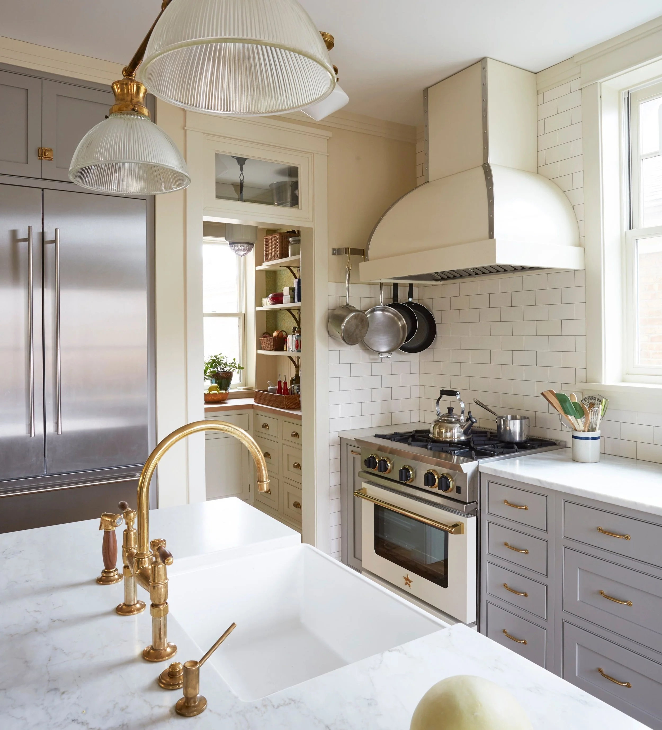 KitchenLab Interiors finished Sunnyside kitchen with light gray kitchen island, white marble countertops, dark maple wood floors, and brass vintage light fixtures