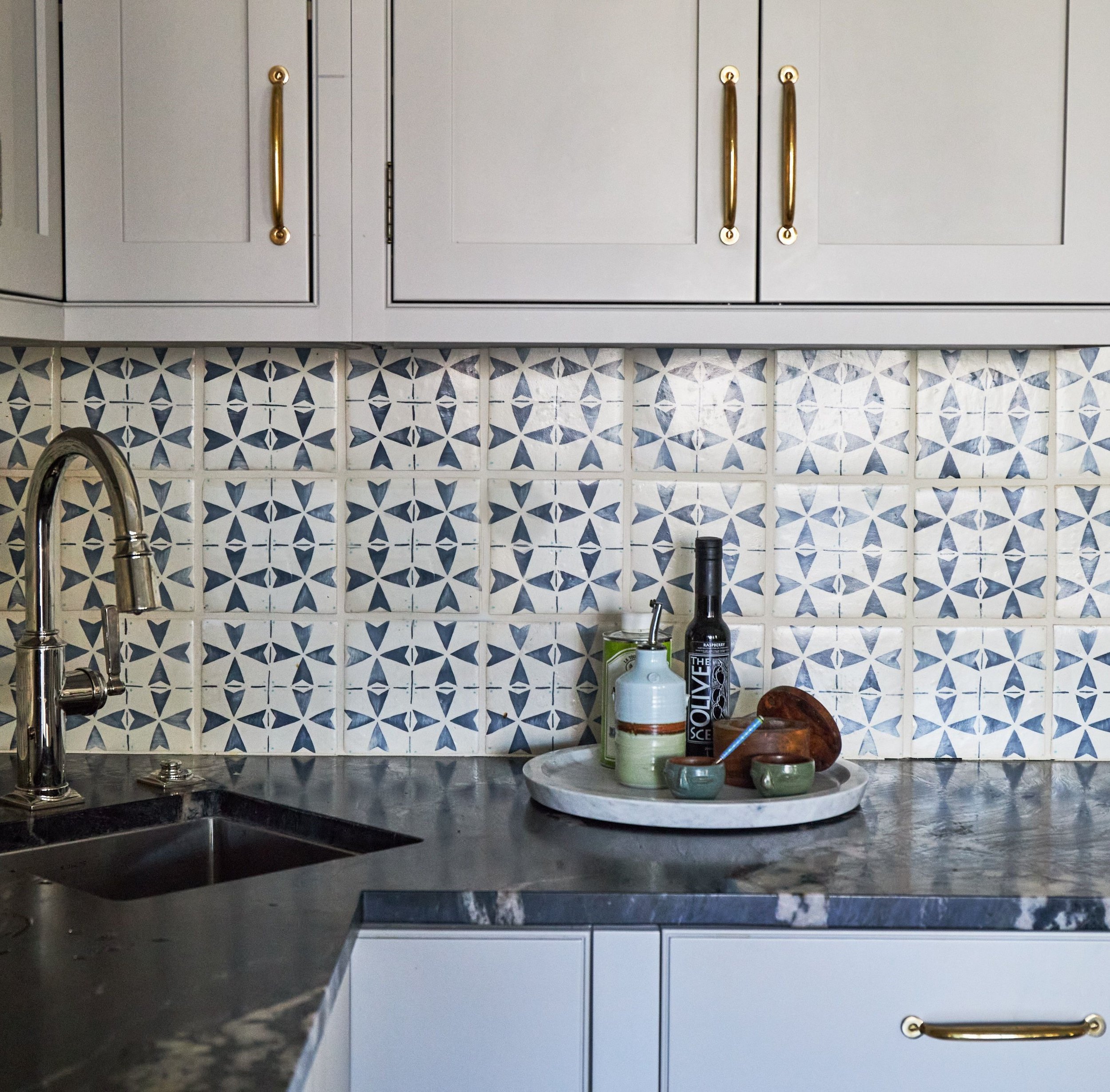 Beautiful navy blue and beige natural tile backsplash with light beige cabinetry and brass antique hardware