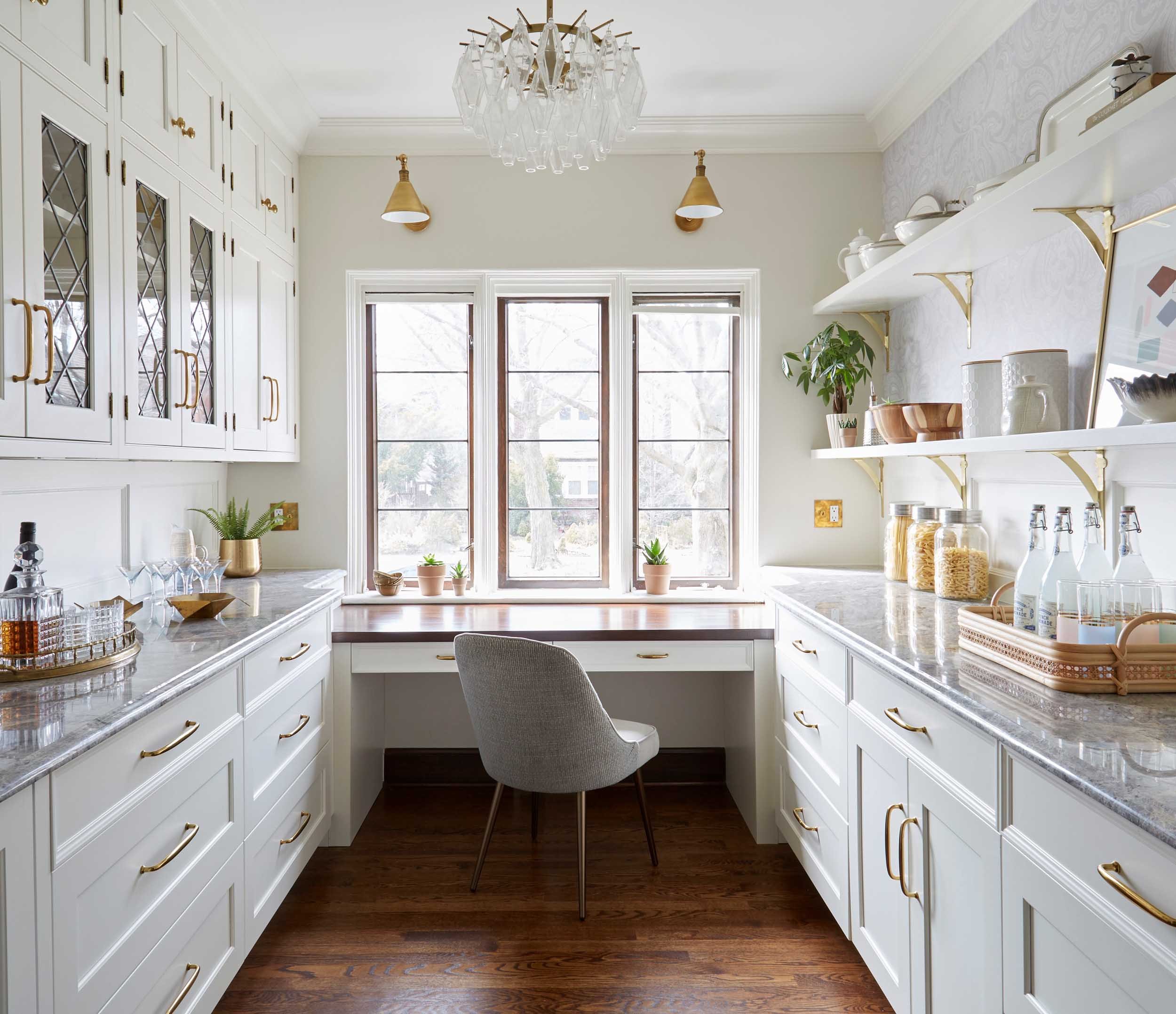 A gorgeous kitchen space with cabinetry, pantry, desk and outdoor window view with glass chandelier