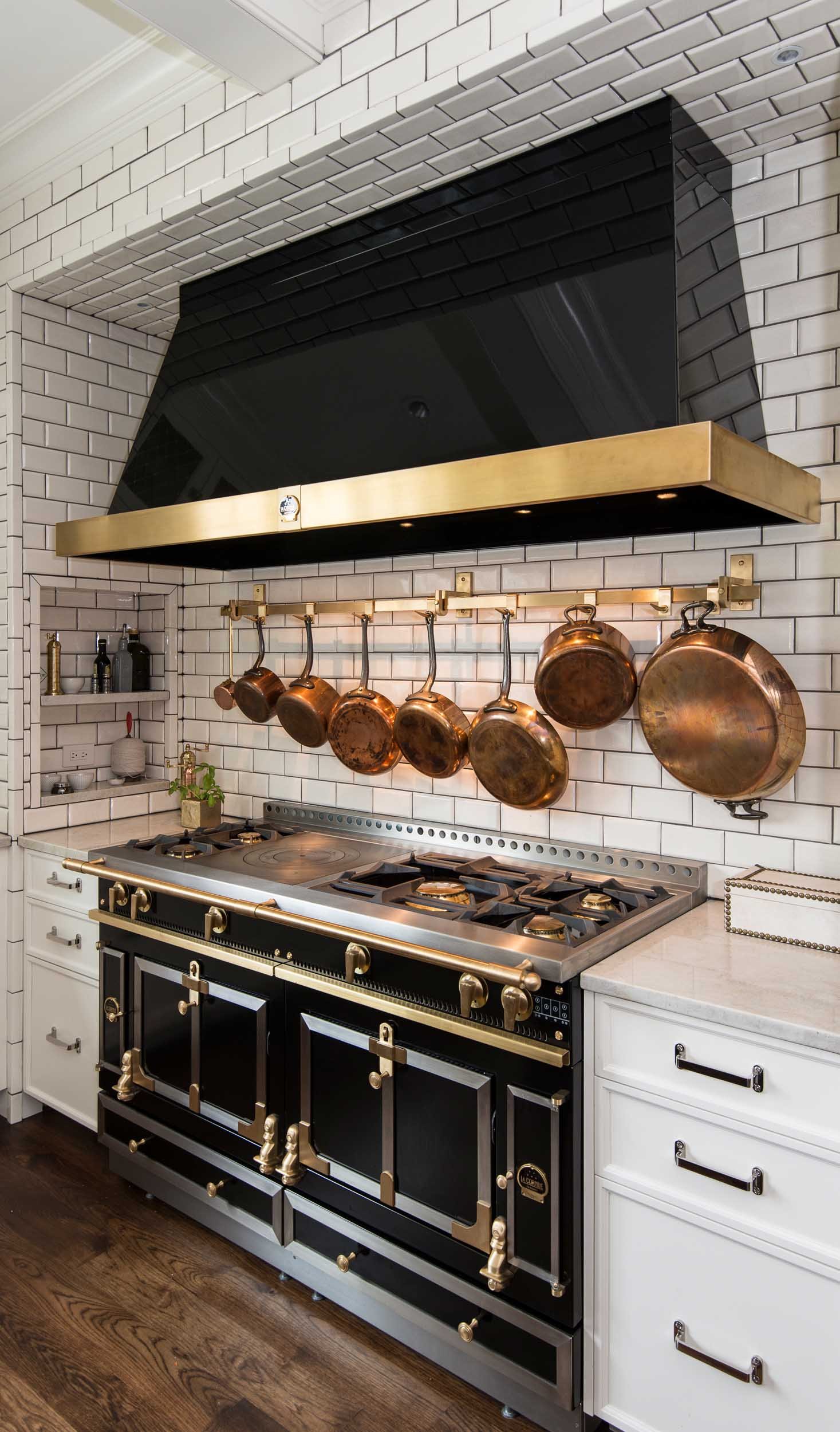 View of copper pots and pans hanging over a high-end range with brass fixtures