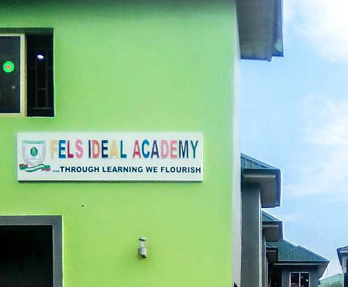 Colorful sign on a green building that reads 'Elsidel Academy' with the slogan 'Through learning we flourish' underneath.