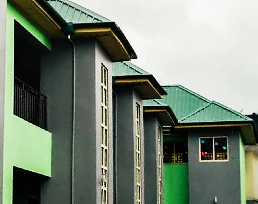 Several modern multi-story buildings with green and gray exteriors, metal roofs, and balconies, under an overcast sky.