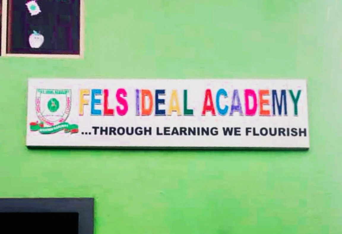 Colorful classroom sign displays 'FELS IDEAL ACADEMY ... THROUGH LEARNING WE FLOURISH' on a green wall.