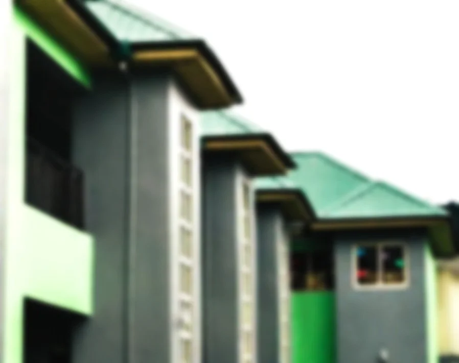 Blurred image of a modern residential building with gray exterior walls, multiple windows, and a green roof.