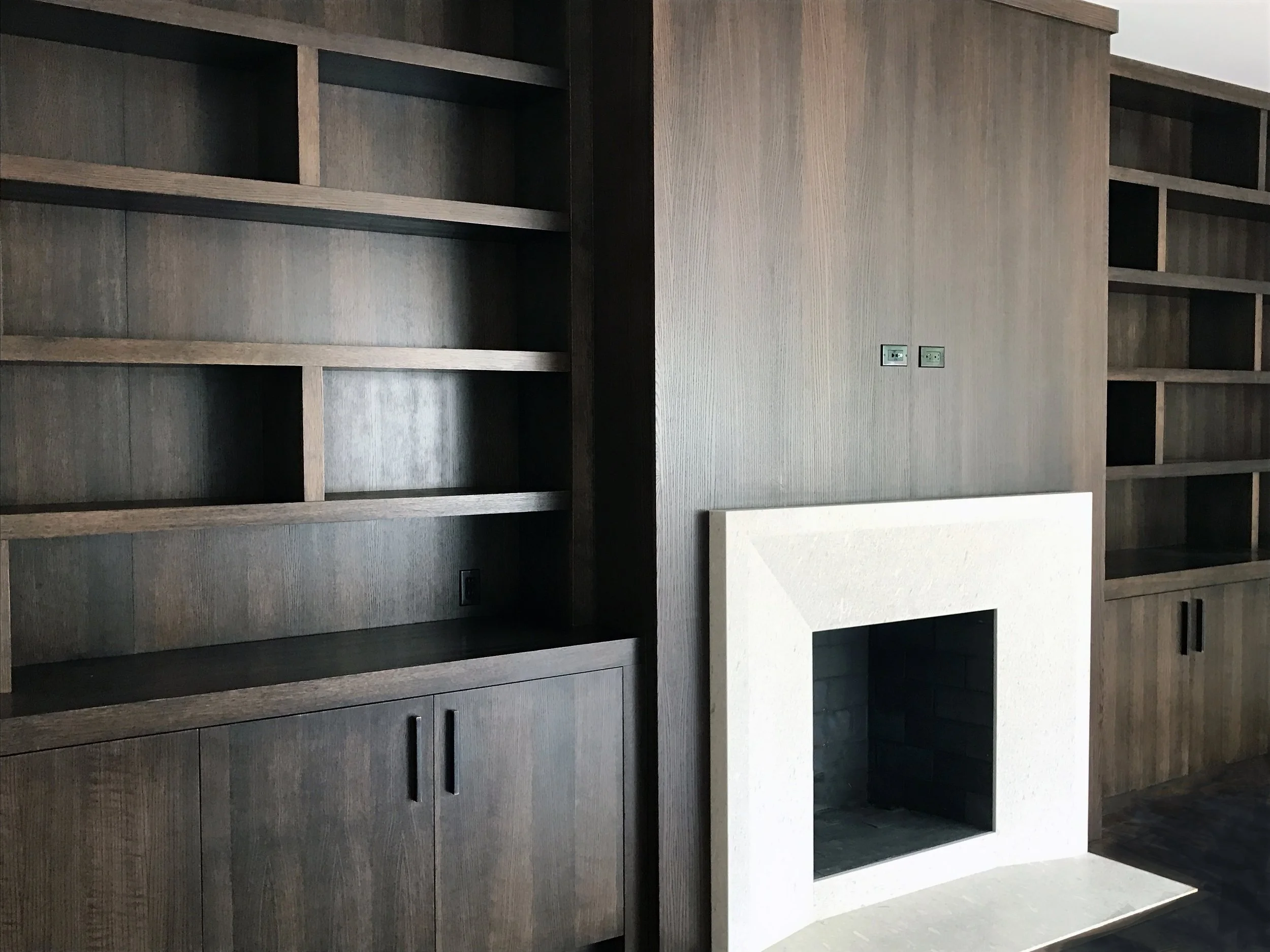 Empty dark wood built-in shelves and cabinets on either side of a white fireplace with a black interior.