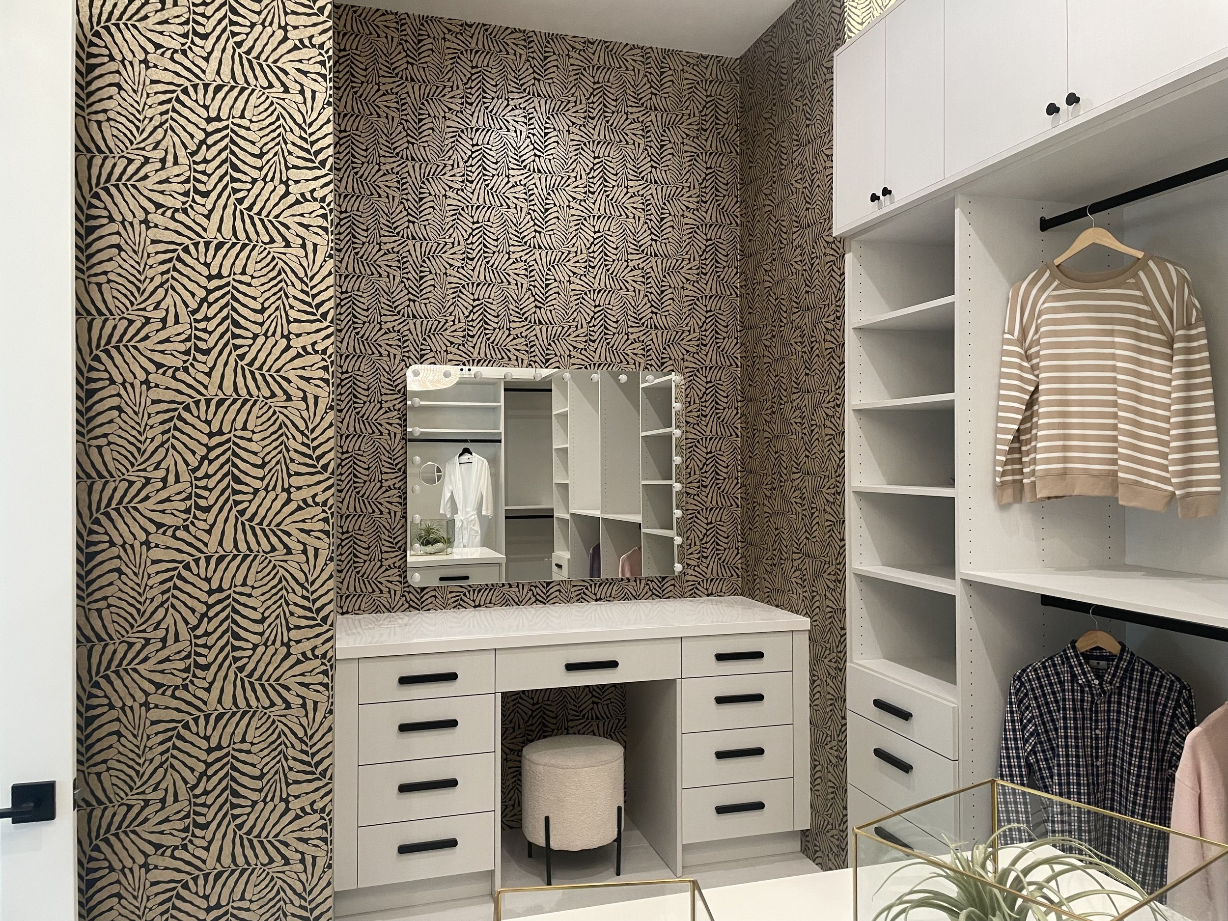 Master walk in closet, custom wall paper, double hang, black hardware, seating makeup area, lit mirror