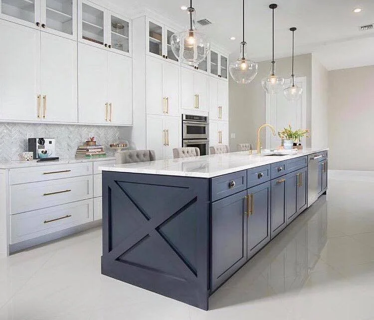 Modern kitchen with white and navy blue cabinetry, gold hardware, marble countertops, pendant lighting, and a built-in oven.