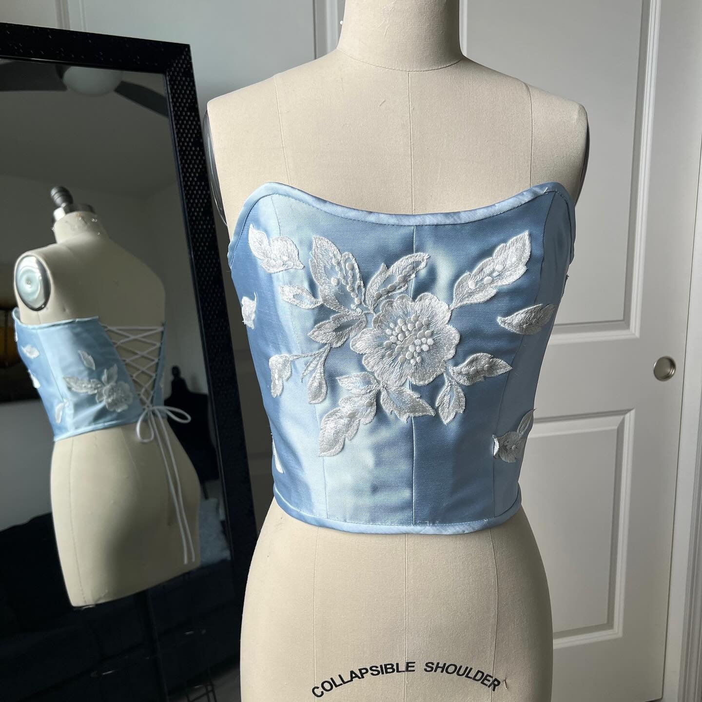 Sky Corset - Made from mikado satin twill and adorned with hand cut floral appliqué, our Sky corset brings “something blue” to your wedding wardrobe.
Shown on mannequin with 36.5” bust, 27.5” waist. Can be laced loose