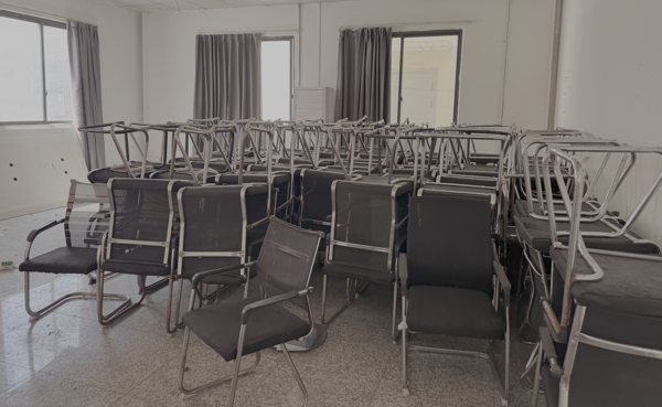 Dozens of office chairs, stacked in a room within an abandoned scam compound.