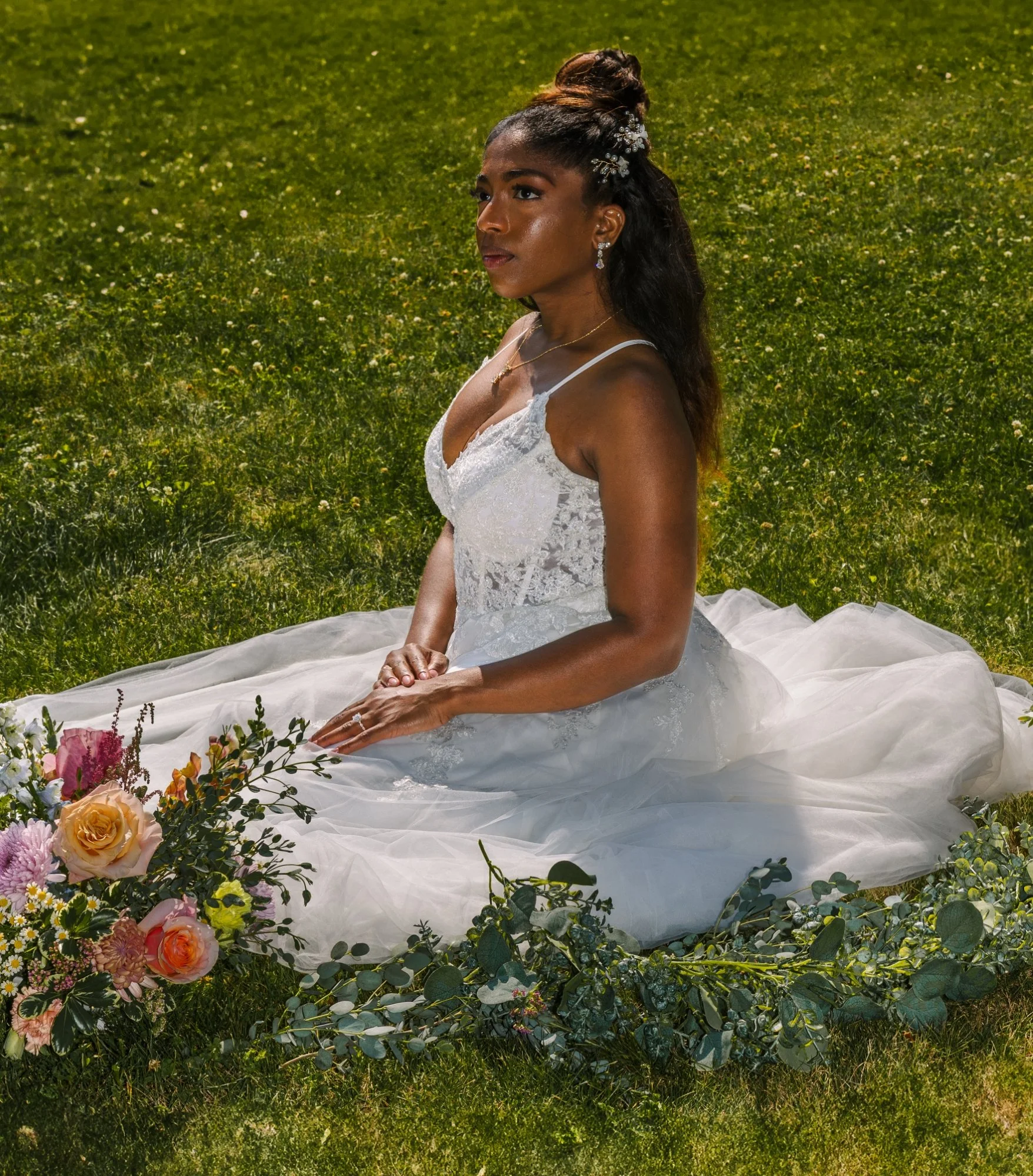 A woman in a white wedding dress sitting on the grass surrounded by flowers.