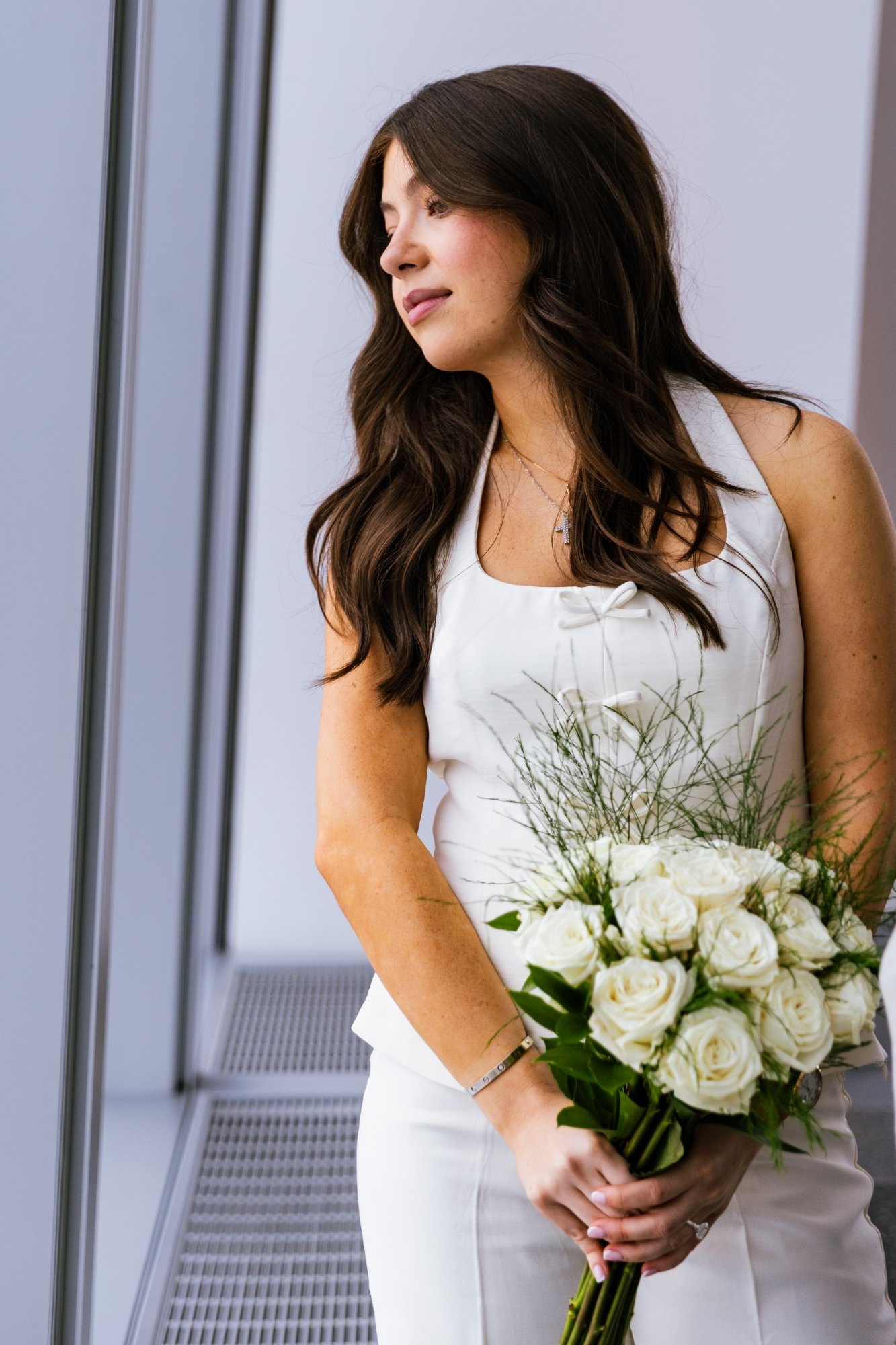 A woman in a white dress holding a bouquet of white roses and greenery.