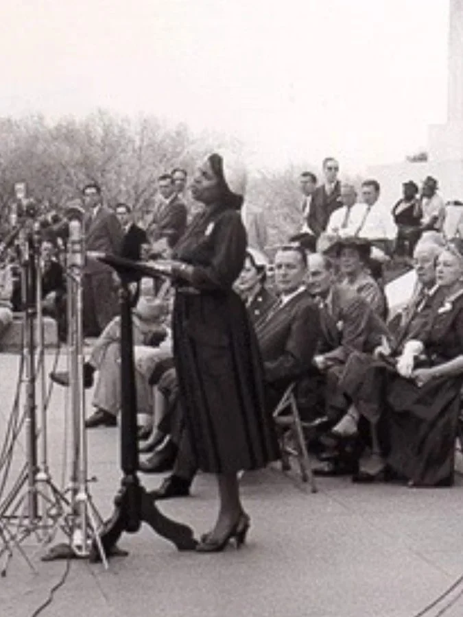 Black-and-white historical photo of Marian Anderson speaking at a podium before a seated audience at the Lincoln Memorial