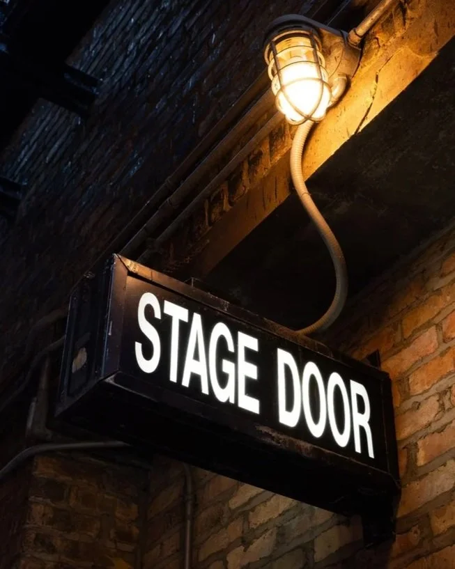 Illuminated stage door sign mounted on a brick theater wall