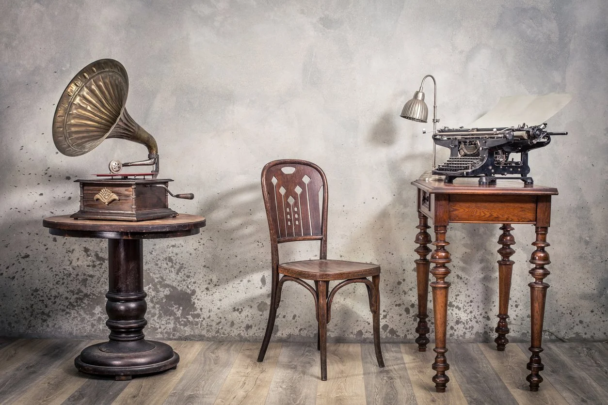 Vintage gramophone, wooden chair, and antique typewriter on a table against a distressed wall